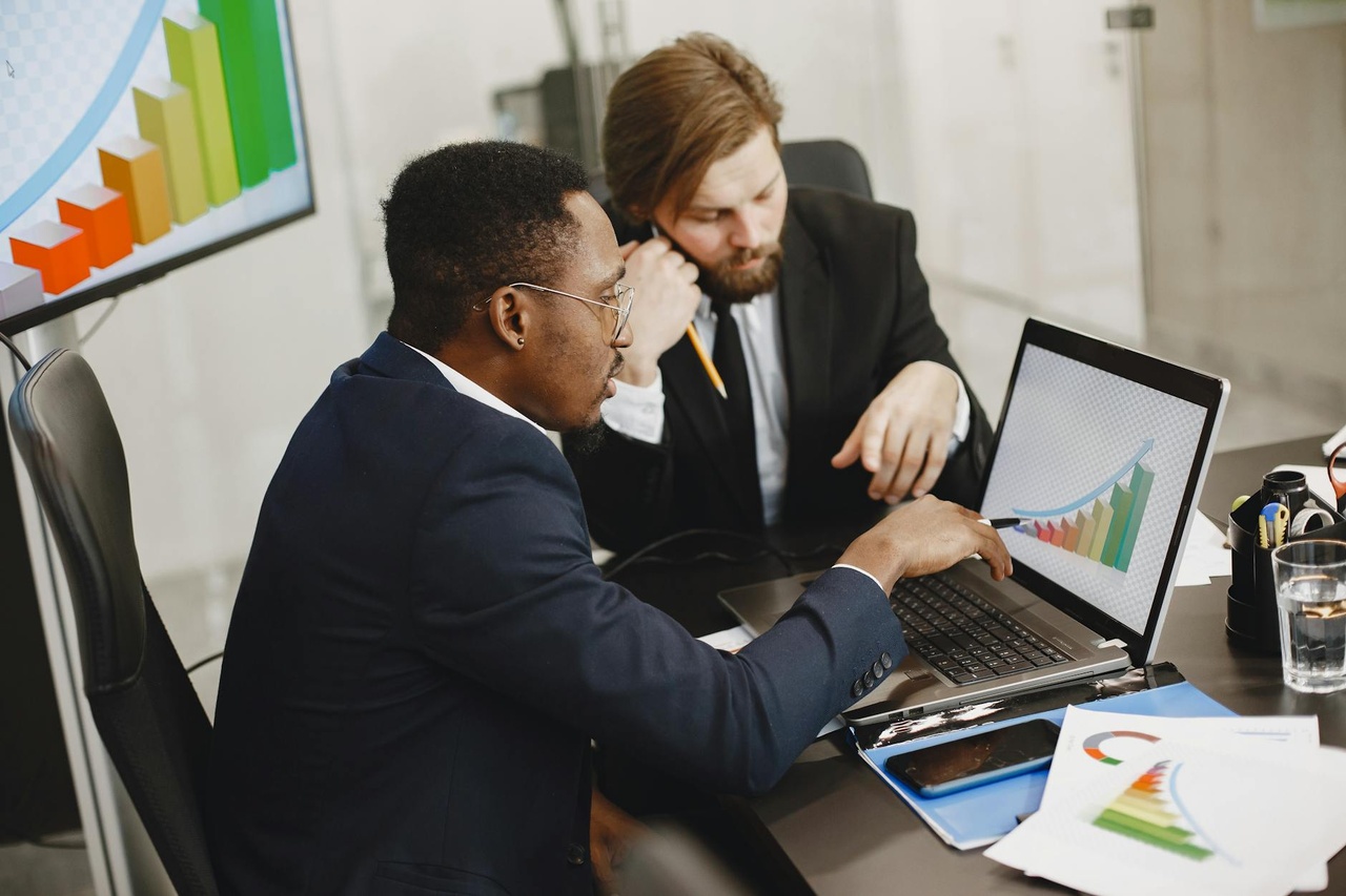 Two business professionals working on growth charts using laptop in an office setting.